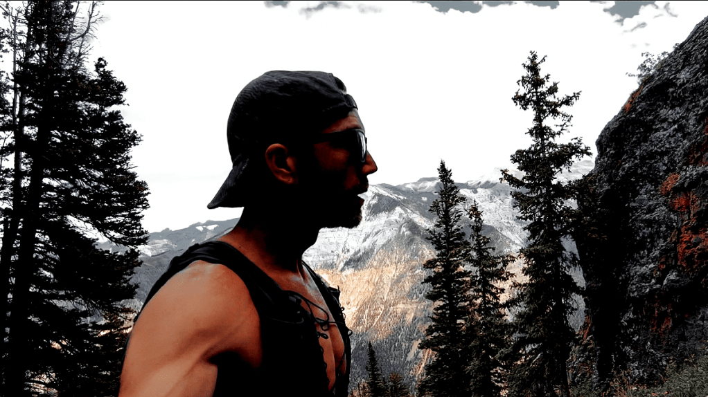 A dramatic image of ultra runner Alex Griffin ascending Twin Peaks in a moody mountainous setting amid pine trees, granite outcroppings, and mountains in the backround