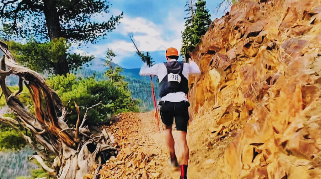 Image of ultra runner Alex Griffin ascending the incredibly difficult Bridge of Heaven section of the Ouray 100 ultramarathon, climbing through the "Blowout" section of the climb, with orange shale, pine trees, and a mountainous backround